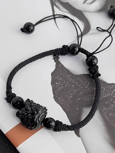 Macro shot of handcrafted black obsidian Pixiu bracelet with woven cord on a magazine