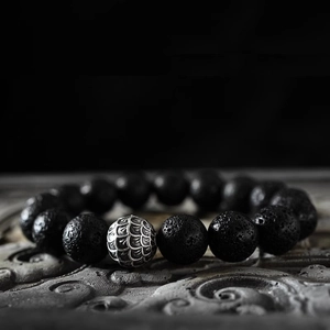 Close-up of black lava stone beads and silver cylinder charm with scale texture