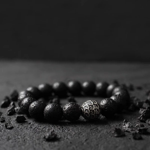 Detailed view of black lava stone beads and antique metallic textured bead on a rock surface