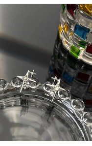 Macro detail of silver star earrings with square crystal on a decorative glass dish