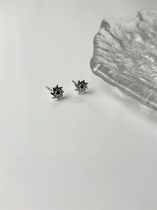 Macro view of silver sunburst gear earrings with a black zircon center on a grey surface