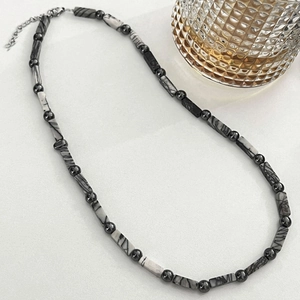 Minimalist textured stone beaded necklace with adjustable silver clasp on a white background