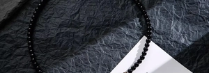 Collana di perle in ossidiana nera lucida da uomo su uno sfondo scuro materico