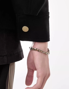 Detail of two-tone woven titanium steel Cuban bracelet on wrist with black sleeve