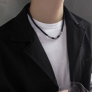 Collana da uomo con perline nere e anelli d'argento indossata da un modello in abito