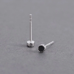 Macro shot of minimalist silver stud earrings with black zircon and crown settings