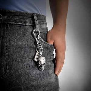 Close-up of vintage silver skull keychain hanging from a grey denim belt loop