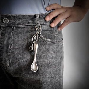 Detail of silver spoon-shaped keychain hanging on grey denim jeans belt loop