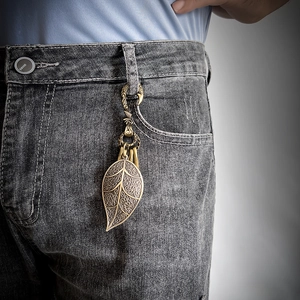 Vintage brass leaf keychain with hollow filigree hanging on denim pants for punk style