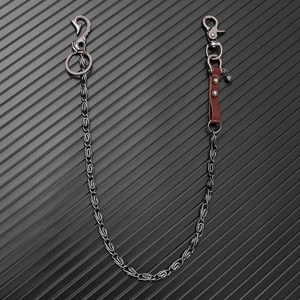Macro detail of punk wallet chain with brown leather trim and metal hooks on black background