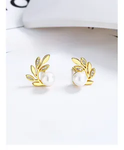 Gros plan de boucles d'oreilles feuilles dorées avec perles blanches et zircons