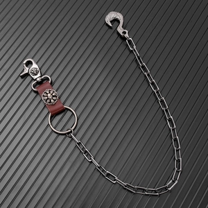 Detail of punk trousers chain with eagle hook, red leather strap and skull metal ornaments