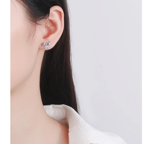 Macro shot of silver bow stud earring with hollow heart patterns on a model ear
