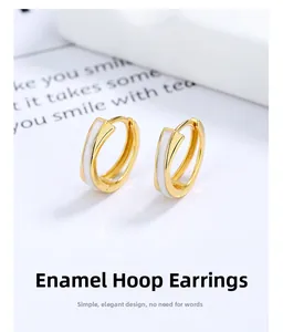 Détail macro de boucles d'oreilles croisées dorées avec émail blanc sur fond blanc