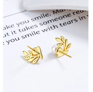 Gros plan sur des boucles d'oreilles feuille d'olivier dorée avec perles blanches