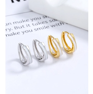 Détails de boucles d'oreilles créoles dorées et argentées avec émail blanc sur fond épuré