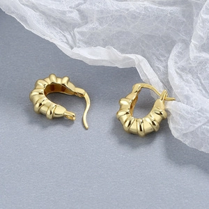 Close-up of golden arch earrings with spiral texture and mirror finish on blue silk