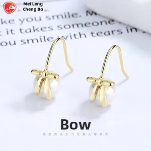 Close-up of golden bow-shaped drop earrings with white pearls on a paper background