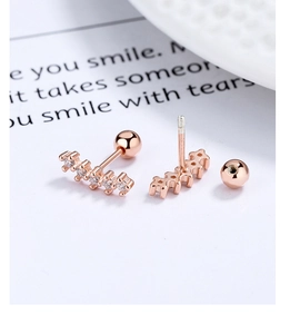 Macro shot of rose gold curved bar earrings with five zircons and screw ball backings