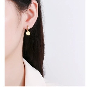 Detailed close-up of a minimalist gold geometric disc hoop earring worn by a model