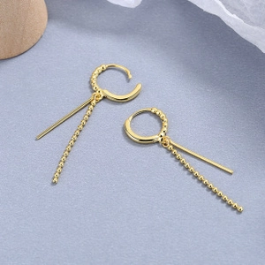 Detail of gold-plated tassel earrings with circular buckle and asymmetric bead chains