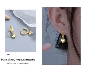 Gros plan de boucles d'oreilles cœur en argent 925 doré portées par un mannequin de mode
