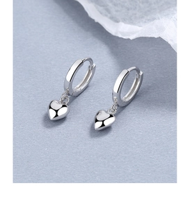 Gros plan de boucles d'oreilles cœur minimalistes en argent 925 sur fond texturé bleu