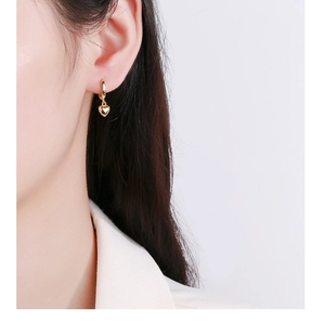 Gros plan de boucles d'oreilles cœur dorées sur modèle montrant la texture polie