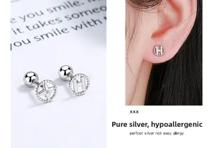Macro detail of 925 sterling silver screw back earrings with H letter and star motifs