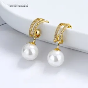 Macro detail of V-shaped gold earrings with paved zircons and hanging round white pearls