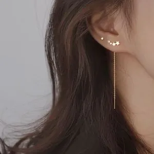 Detail of elegant gold star-shaped stud and long tassel earrings on model ear