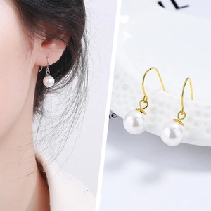 Détail de longues boucles d'oreilles en perles dorées portées et sur surface blanche