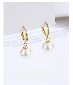 Detailed view of teardrop pearl earrings with gold U-shaped hoops and micro-diamonds
