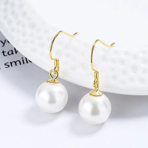 Close-up of elegant gold hook earrings with round white pearls on a minimalist background