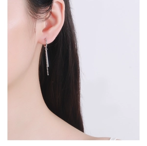 Close-up of silver tassel earrings with a sleek metal bar and delicate ball chain on a model