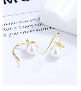 Macro shot of elegant gold bow earrings with round white pearls and 925 silver hooks