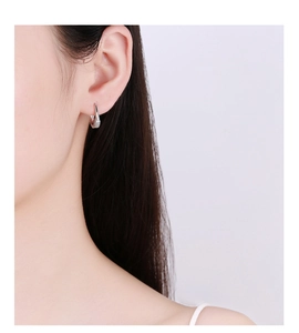 Makroaufnahme von silbernen Creolen mit Zirkonia-Mikropavé direkt am Ohr getragen