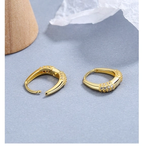 Detailansicht goldener Creolen mit Mikro-Pavé-Zirkon-Inlay auf grauem Hintergrund