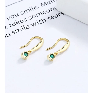 Macro detail of gold-plated hook earrings featuring polished emerald green round crystals