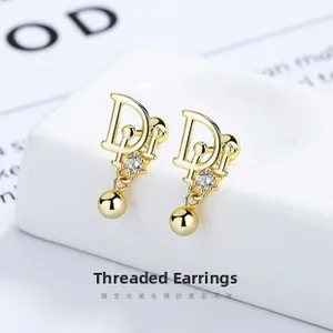 Detail of gold letter D earrings with zircon inlay and smooth metal beads on white stand