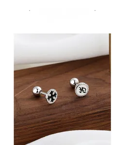 Detail view of 925 silver cross screw earrings with black drip oil on dark wood surface