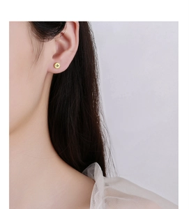 Close-up of a minimalist round gold ear stud with black artistic symbols on a female model