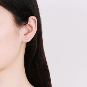 Minimalist silver star stud earring with tiny smiley face shown on a model earlobe