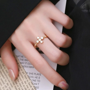 Close-up of a gold cross ring with five white cubic zirconia stones worn on finger