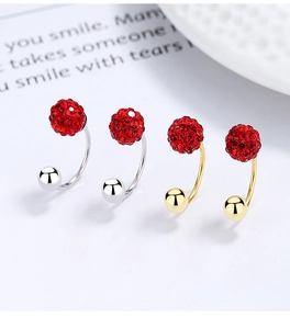 Detail of four C-shaped silver and gold earrings with red disco ball crystals on white