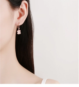 Détail de boucles d'oreilles trèfle rose avec crochet or rose portées par un modèle