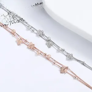 Detail view of double-layer silver and rose gold bracelets with maple leaf charms