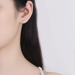 Close-up of a silver teddy bear stud earring with a pink gem on a model's ear