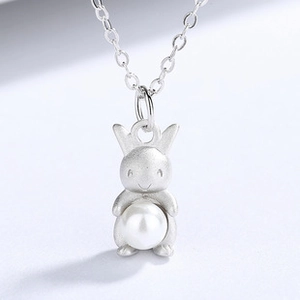 Vue macro d'un pendentif lapin en argent mat tenant une perle blanche sur une fine chaîne