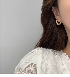 Close-up of model wearing twisted golden rope hoop earrings with white lace top